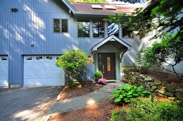 entrance to property featuring a garage, driveway, and a shingled roof