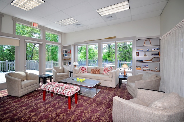 living area with a drop ceiling, visible vents, and a wealth of natural light