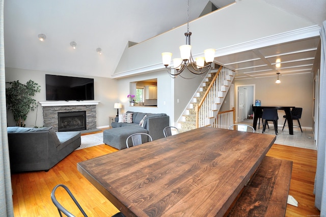 dining area with stairway, an inviting chandelier, light wood-style flooring, lofted ceiling, and a fireplace