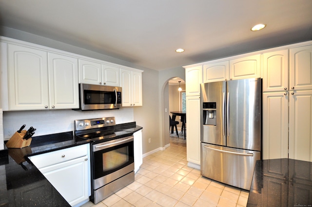 kitchen with dark stone counters, arched walkways, white cabinets, appliances with stainless steel finishes, and backsplash