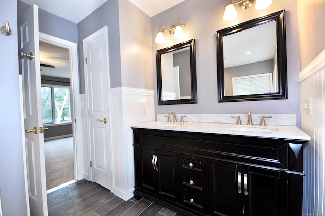 full bath with a sink, a wainscoted wall, wood finished floors, and double vanity