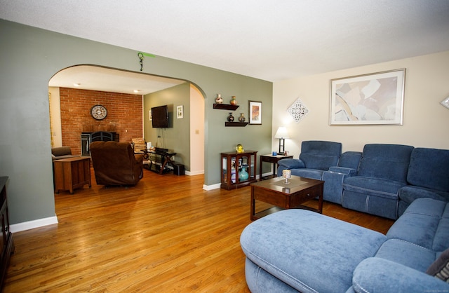 living area featuring a brick fireplace, light wood-style flooring, baseboards, and arched walkways