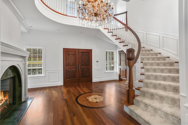 foyer featuring wood finished floors, a warm lit fireplace, stairs, a decorative wall, and a notable chandelier