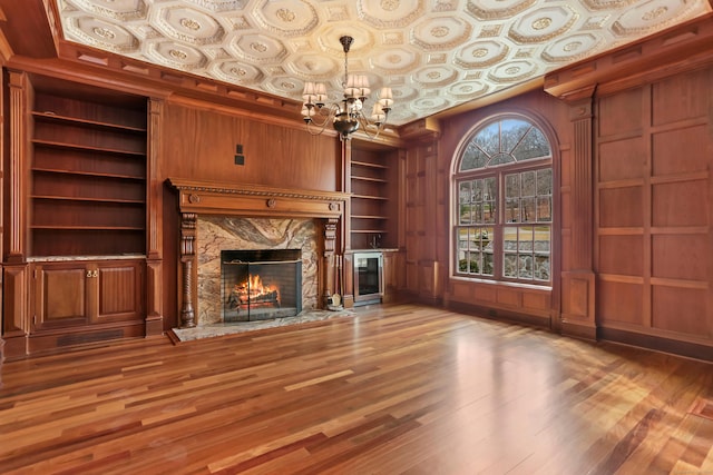 unfurnished living room featuring built in features, wood finished floors, a fireplace, an ornate ceiling, and a chandelier