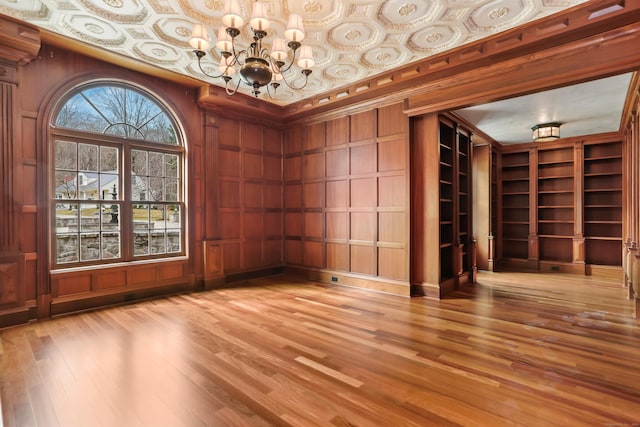 empty room featuring wooden walls, an inviting chandelier, and light wood-style flooring