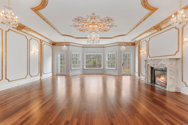 unfurnished living room with a raised ceiling, a notable chandelier, a fireplace, and wood finished floors