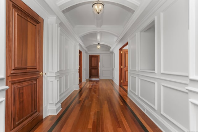 corridor with vaulted ceiling, a decorative wall, arched walkways, and dark wood-style flooring