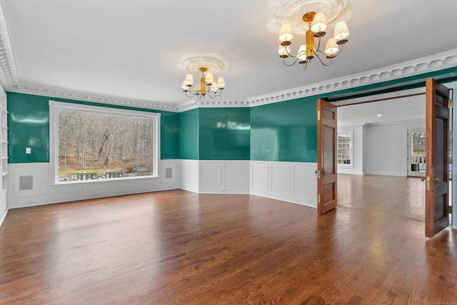 spare room with a notable chandelier, wainscoting, ornamental molding, and wood finished floors