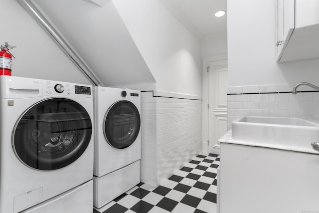 washroom with light floors, washer and dryer, cabinet space, tile walls, and a sink