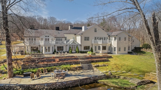 back of property featuring a lawn, a fire pit, a balcony, a chimney, and a patio area