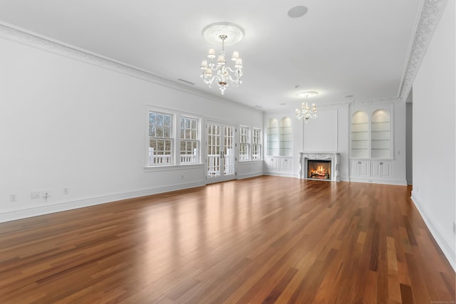 unfurnished living room with built in features, wood finished floors, an inviting chandelier, a fireplace, and baseboards