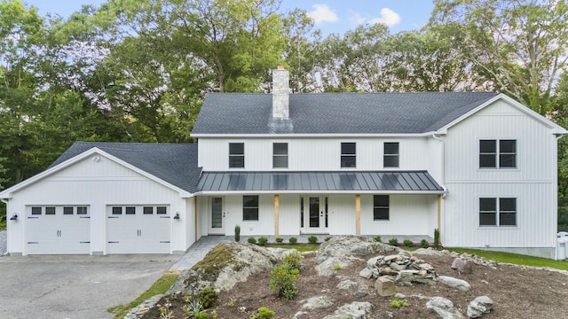 modern farmhouse featuring metal roof, a porch, aphalt driveway, an attached garage, and a chimney