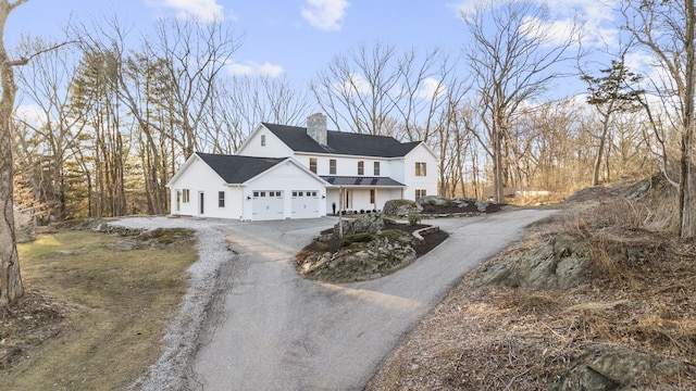 modern farmhouse with aphalt driveway, a chimney, and an attached garage