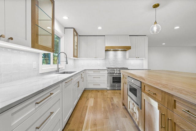 kitchen with light stone counters, custom exhaust hood, a sink, built in microwave, and high end range