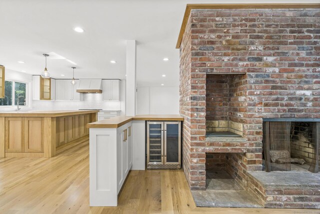 kitchen featuring light wood-style floors, wine cooler, a brick fireplace, a sink, and exhaust hood