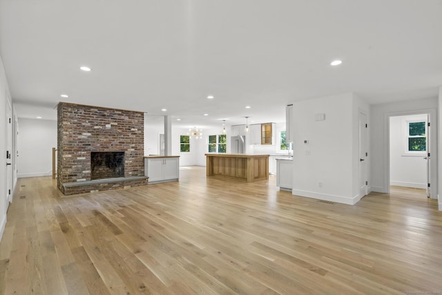 unfurnished living room featuring recessed lighting, a brick fireplace, light wood-style flooring, and baseboards