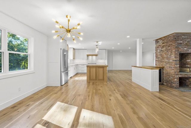 kitchen with a center island, light wood finished floors, high end fridge, a sink, and a chandelier