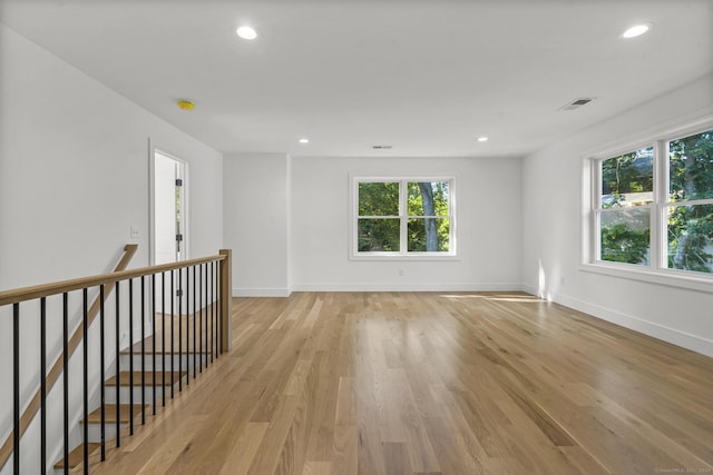 spare room featuring baseboards, light wood-type flooring, visible vents, and a healthy amount of sunlight