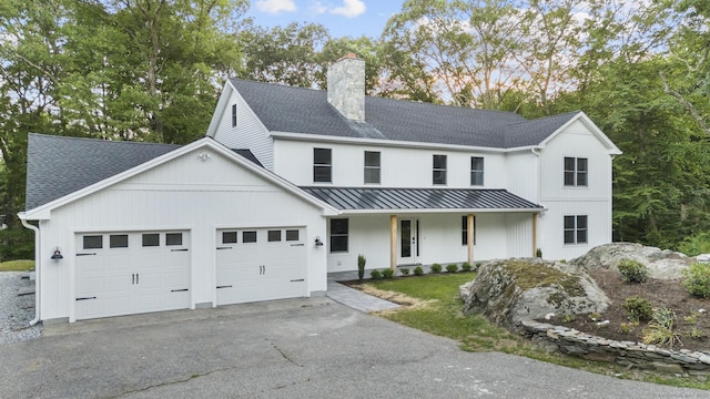 modern farmhouse style home featuring a garage, a standing seam roof, a shingled roof, and a chimney