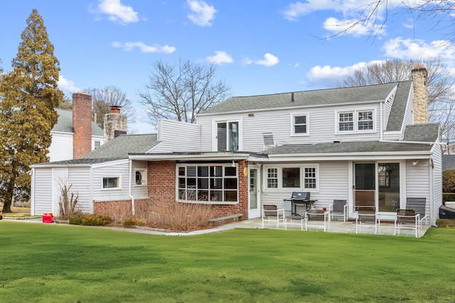 back of property with a yard, a chimney, and a patio