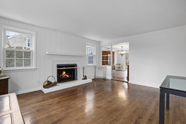 unfurnished living room with baseboards, a fireplace, hardwood / wood-style flooring, and an inviting chandelier