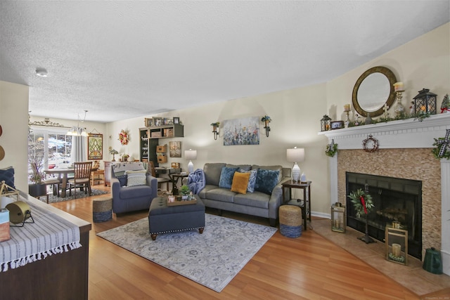 living area with a tile fireplace, a notable chandelier, a textured ceiling, and light wood finished floors