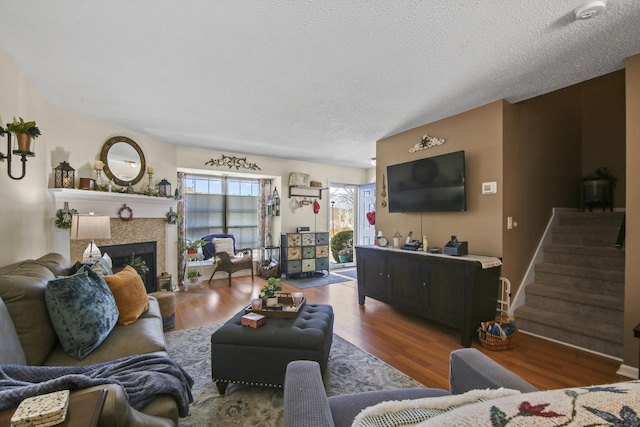 living area featuring a textured ceiling, stairway, a fireplace, and wood finished floors