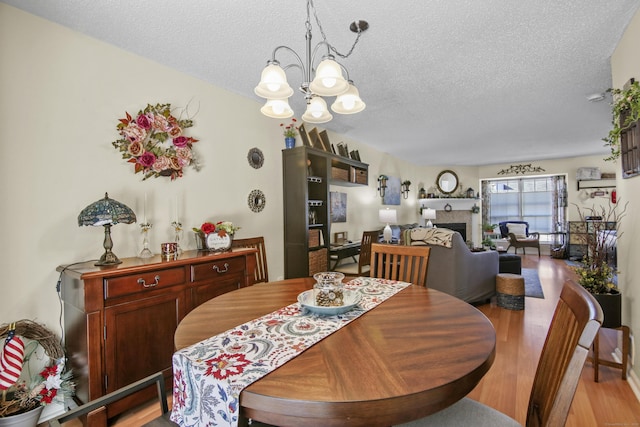 dining space with light wood-type flooring, an inviting chandelier, a textured ceiling, and a tiled fireplace