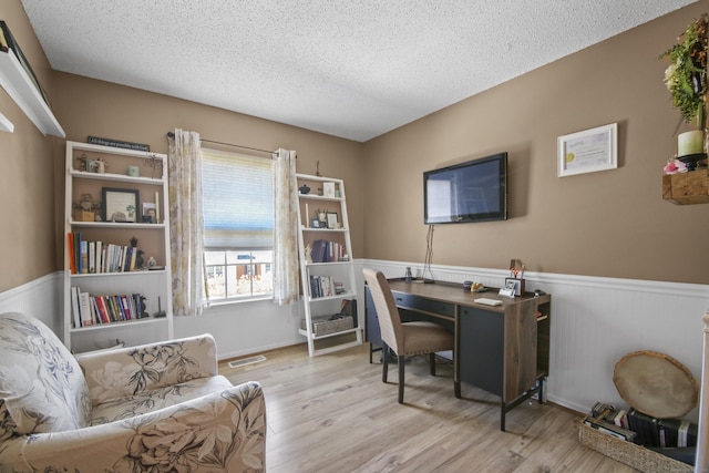 home office with a textured ceiling, visible vents, wood finished floors, and wainscoting