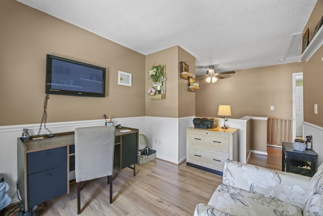 office space with light wood-type flooring, a ceiling fan, a textured ceiling, and wainscoting