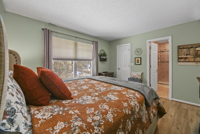 bedroom featuring a textured ceiling, ensuite bath, wood finished floors, and baseboards