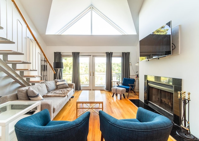 living area featuring stairway, wood finished floors, high vaulted ceiling, a fireplace, and french doors