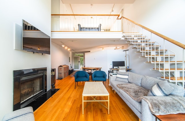 living area featuring stairway, a fireplace, a towering ceiling, and wood finished floors