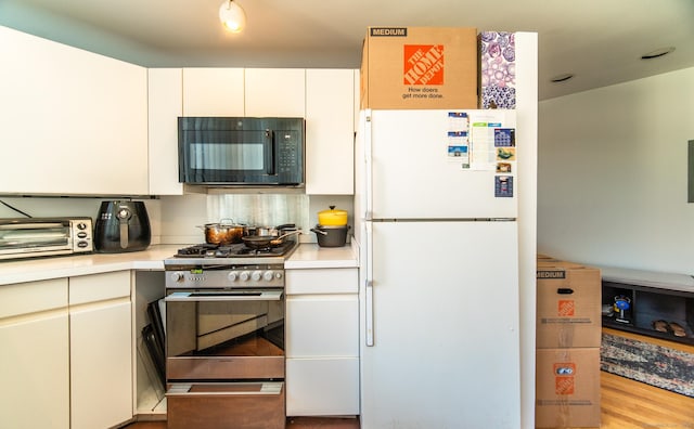 kitchen featuring black microwave, a toaster, stainless steel range with gas stovetop, light countertops, and freestanding refrigerator