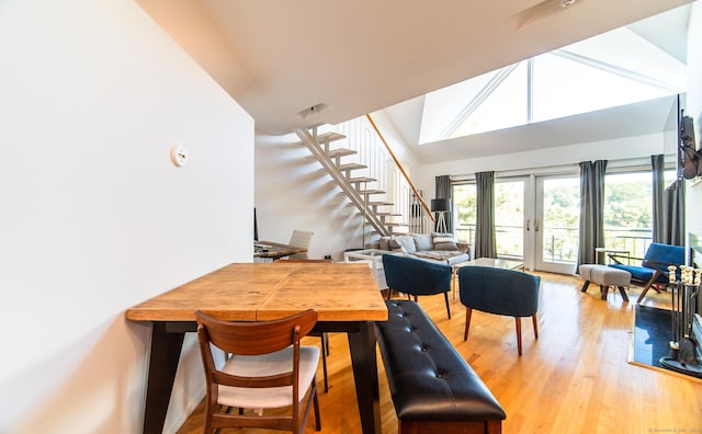 dining space with french doors, lofted ceiling, light wood-style floors, and stairs