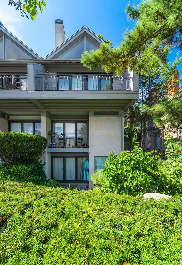 back of property featuring stucco siding, a balcony, and a chimney