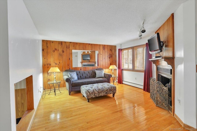 living area featuring light wood-style flooring, a textured ceiling, wood walls, a fireplace, and a baseboard radiator