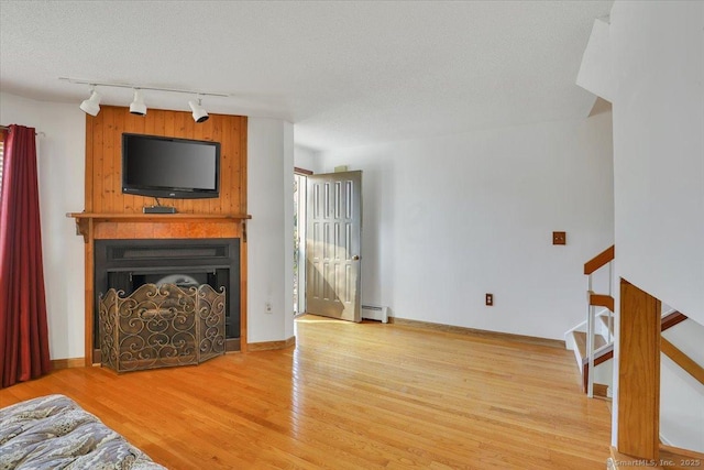 living area with stairway, baseboard heating, a fireplace, wood finished floors, and a textured ceiling