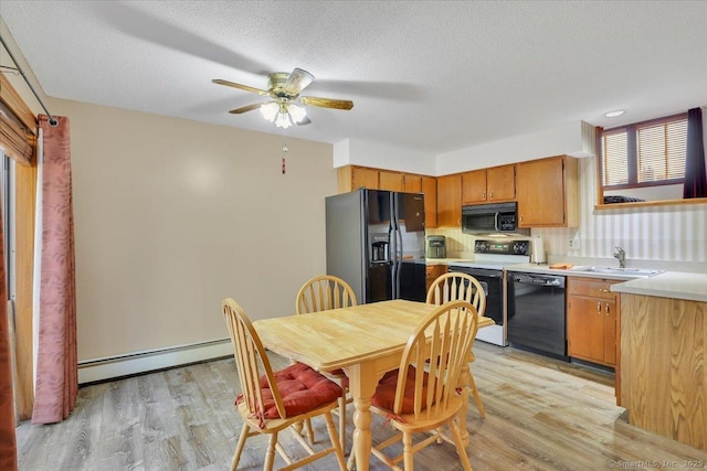 kitchen with a sink, baseboard heating, black appliances, and light wood finished floors