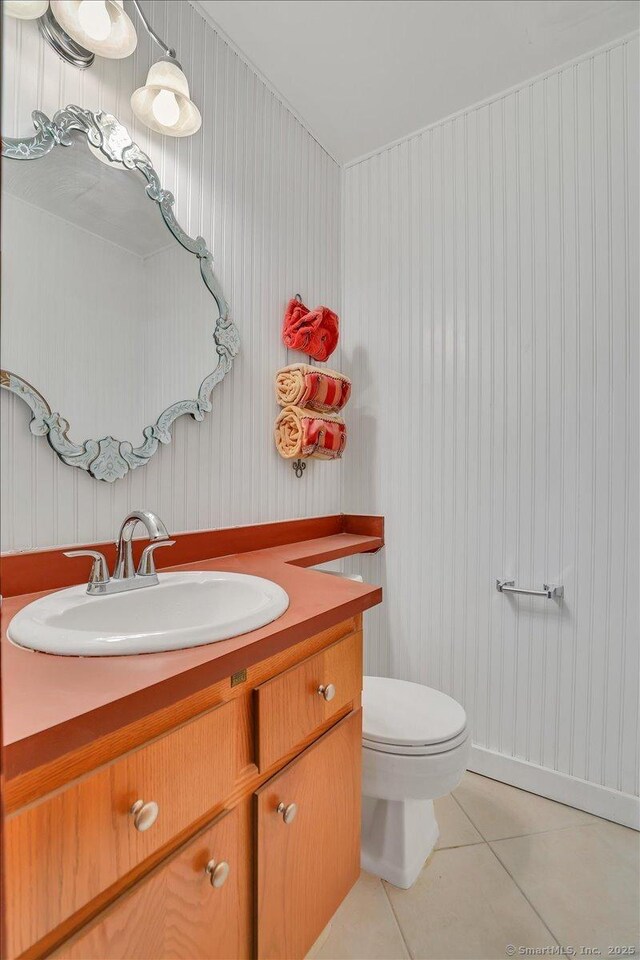 half bath featuring tile patterned flooring, toilet, and vanity