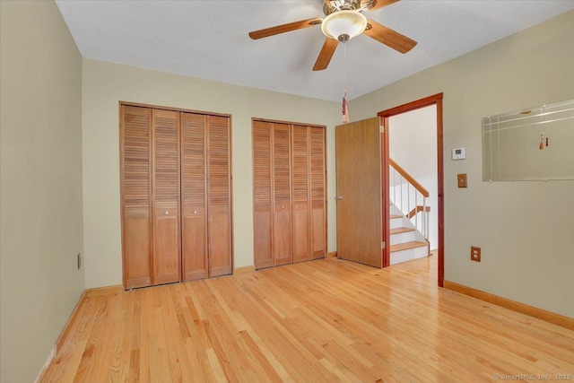 unfurnished bedroom featuring light wood-type flooring, multiple closets, baseboards, and ceiling fan