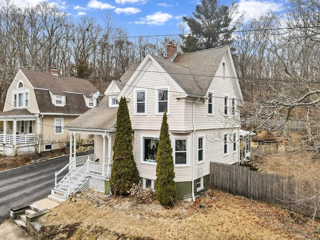 view of front facade featuring a porch, roof with shingles, a chimney, and fence