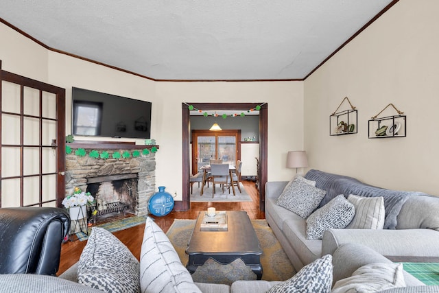 living area featuring baseboards, wood finished floors, a stone fireplace, crown molding, and a textured ceiling