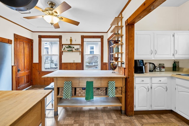 kitchen with wainscoting, wooden walls, white cabinetry, and refrigerator