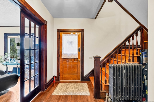 foyer entrance with baseboards, radiator heating unit, wood-type flooring, stairs, and french doors