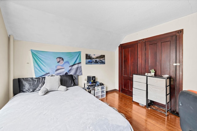 bedroom with dark wood-type flooring, vaulted ceiling, a textured ceiling, and baseboards