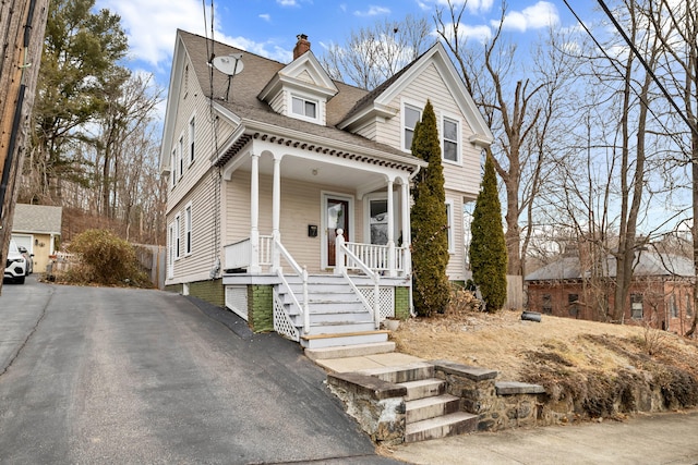 view of front facade featuring a porch, a shingled roof, and a chimney