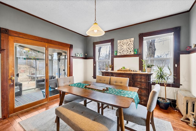 dining room with radiator heating unit, ornamental molding, light wood-style flooring, and a textured ceiling