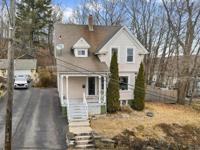 view of front of house with covered porch, driveway, roof with shingles, and fence