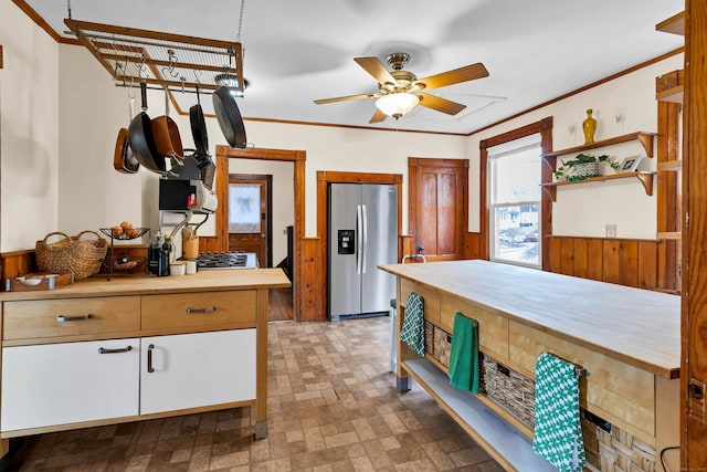 kitchen with a wainscoted wall, crown molding, open shelves, a ceiling fan, and stainless steel fridge with ice dispenser